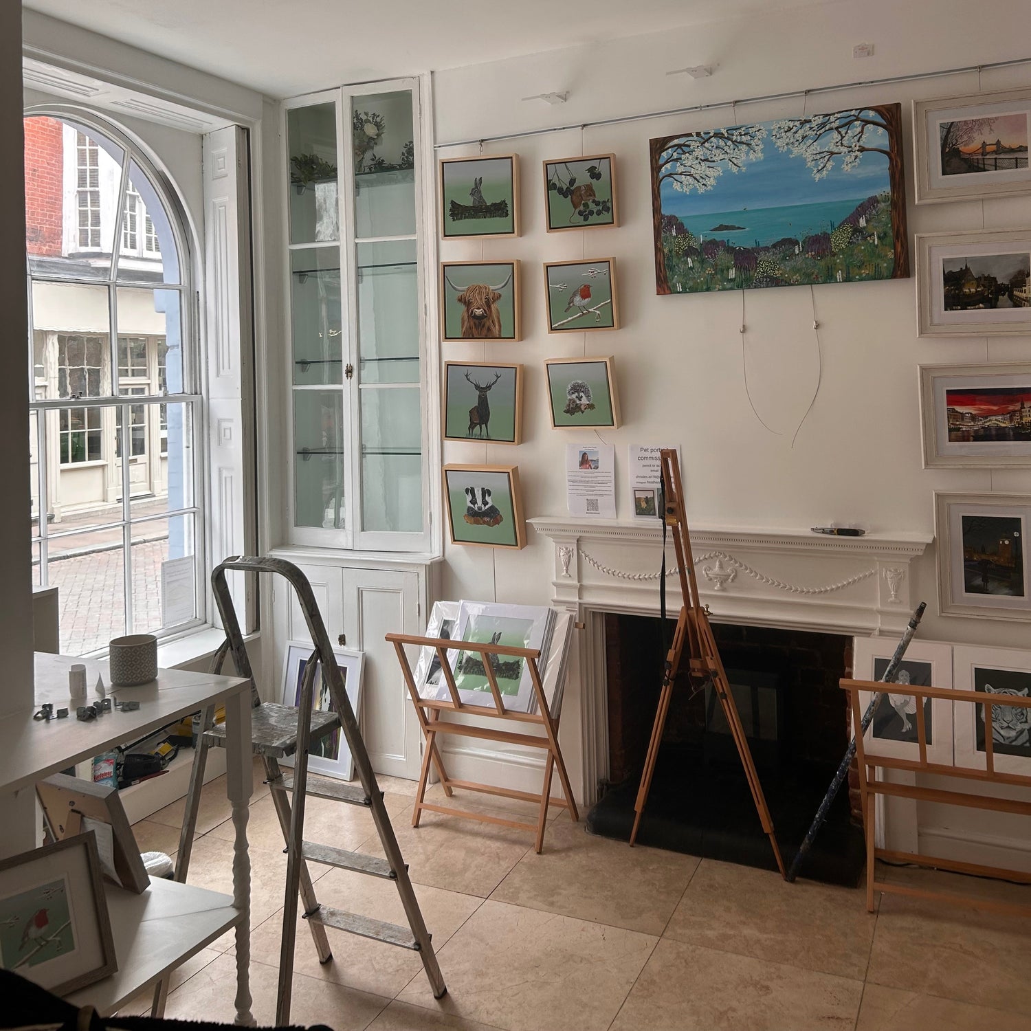Gallery setup in progress with a wall of framed pictures and a fireplace